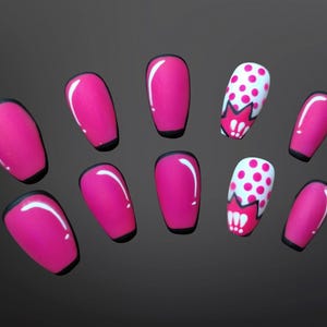 May include: A set of ten artificial nails in a pop art style. The nails are primarily hot pink with a black outline. Two nails feature a white base with pink polka dots and a red and white graphic.