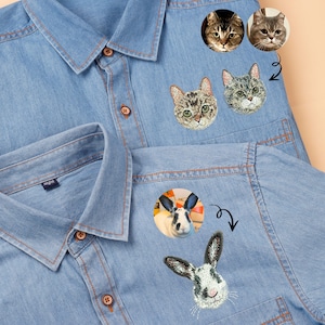 May include: Light blue denim shirts featuring embroidered cat and rabbit faces. The shirts have button fastenings and collars. The cat and rabbit faces are in a circular design, with the rabbit face below the cat faces.