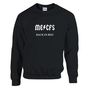 Op de afbeelding: Zwart sweatshirt met witte tekst die "me/cfs BACK IN BED" in een rockband-lettertype leest.