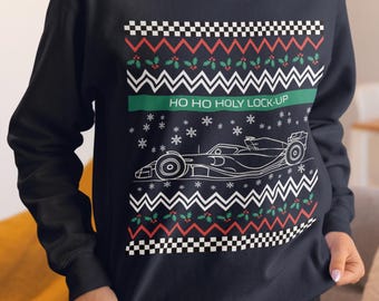 May include: Navy blue sweatshirt with a festive design. The design includes a Formula 1 race car outline, snowflakes, and the text "HO HO HOLY LOCK-UP" in white and green. The top border has a black and white checkered pattern.