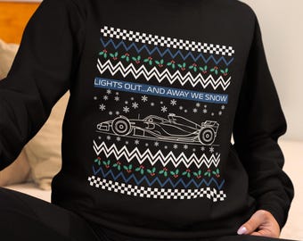 May include: Black sweatshirt with a festive design. The design includes a Formula 1 race car, snowflakes, and the text "LIGHTS OUT...AND AWAY WE SNOW". The design also features a pattern of white zigzags, blue and green holly, and checkered patterns.