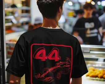May include: Black t-shirt with a red graphic featuring the number "44" and a race car design. The design is enclosed in a red rectangular frame. The person is standing in front of a glass display case.