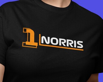 May include: Black t-shirt featuring the text "1 NORRIS" in orange and white. The number 1 is in an orange box. The word "NORRIS" is in white with an orange underline. The shirt is being worn.