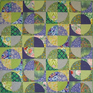May include: A colorful patchwork quilt with a geometric design. The quilt features quarter-circle patterns in shades of green, purple, blue, and yellow. The fabrics include floral, paisley, and striped patterns, creating a vibrant and textured appearance.