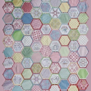 Könnte beinhalten: Ein Quilt bestehend aus zahlreichen sechseckigen Stoffstücken in verschiedenen Pastellfarben und Mustern. Viele der Stoffstücke zeigen aufwendige Stickereien, darunter florale Motive, Haushaltsgegenstände und kleine Tiere, die in einem Wabenmuster zusammengesetzt sind.