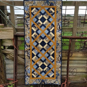 May include: A blue and gold table runner with a geometric pattern. The runner is made of fabric and has a fringed edge.