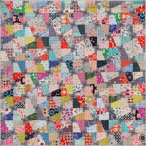 Op de afbeelding: Een kleurrijk patchwork-deken met een zwart-wit geometrisch patroon. Het deken is gemaakt van veel verschillende stoffen en kleuren, waaronder rood, blauw, groen, geel en roze.
