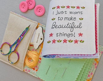 May include: A white fabric sewing kit with a pink and green embroidered quote that reads "I just want to make beautiful things!" The kit includes a pair of rainbow-colored scissors, a small yellow spool of thread, a needle minder, and a green felt pad with needles.