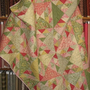 Puede incluir: Colcha hecha a mano con diseño de patchwork. La colcha presenta una variedad de telas en tonos verdes, rosas, rojos y crema, dispuestas en un patrón geométrico. La colcha es probablemente de algodón y tiene una textura suave y acolchada.