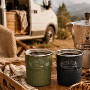May include: Two stainless steel tumblers with a textured lower half, one olive green and one matte black. The green tumbler features a mountain graphic and the text "Olivia est. 2026". The black tumbler features a mountain graphic and "The Anderson Family WANDER TOGETHER".