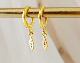 May include: Gold hoop earrings with a dangling leaf-shaped charm featuring a small clear stone.