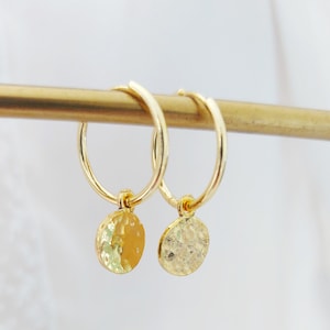 Peut inclure: Une paire de boucles d'oreilles créoles en or avec de petits pendentifs ronds martelés.