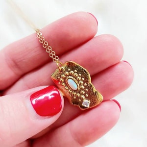Peut inclure: Collier en chaîne dorée avec un pendentif en or texturé orné d'une opale ovale et d'un petit strass transparent.