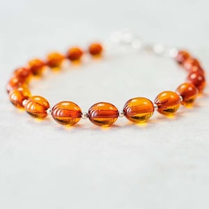 May include: A bracelet made of amber beads with silver spacers. The beads are oval shaped and have a warm, honey-like color.