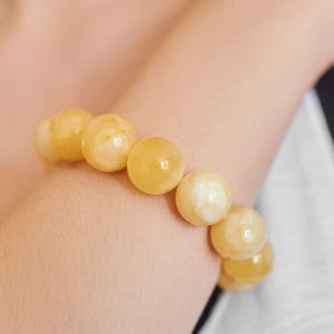 Op de afbeelding: Een armband bestaande uit grote, bolvormige kralen in amberkleuren. De kralen vertonen een gemarmerd effect, met kleuren variërend van crèmewit tot een diepe, gouden tint. De armband wordt om de pols gedragen.