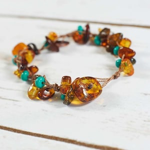 May include: A brown cord bracelet with amber and turquoise beads. The amber beads are various shapes and sizes, some with inclusions.