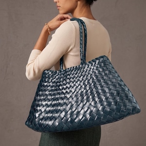 May include: A large, dark blue tote bag featuring an intricate woven pattern across its entire surface. The bag includes two matching braided shoulder straps and a spacious, rectangular silhouette, crafted with a uniform, glossy finish.