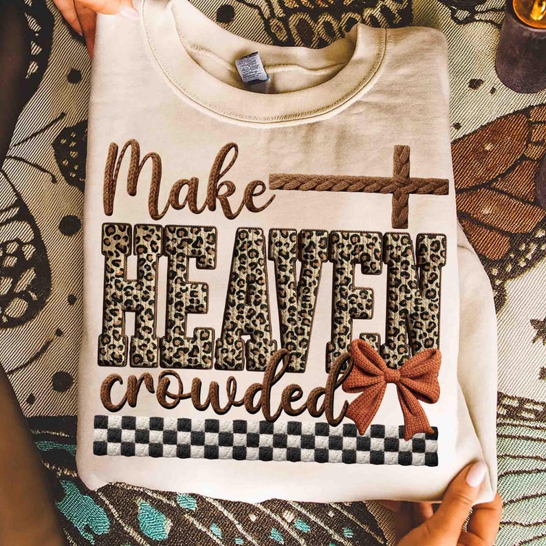 May include: Cream-colored sweatshirt with the text "Make HEAVEN crowded" in brown and leopard print. A brown cross and bow accent the design. A black and white checkered pattern is at the bottom.