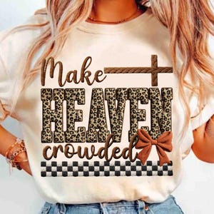 May include: Cream-colored t-shirt with the phrase "Make HEAVEN crowded" in brown and leopard print lettering. A brown cross and bow accent the design, with a black and white checkered border at the bottom. A casual, faith-based tee.