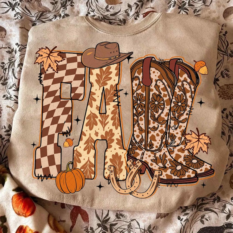 May include: Beige sweatshirt featuring a fall-themed design. The word "FALL" is displayed with a checkered "F", a leaf-patterned "A", and two cowboy boots. A cowboy hat, pumpkin, acorns, and horseshoes complete the design.