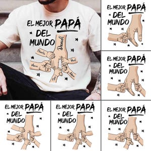 Può includere: T-shirt color crema con la scritta in spagnolo "EL MEJOR PAPÁ DEL MUNDO" (Il miglior papà del mondo). Il design presenta la mano di un padre che tiene le mani di diversi bambini, con nomi come Daniel, Charlie e Paul.