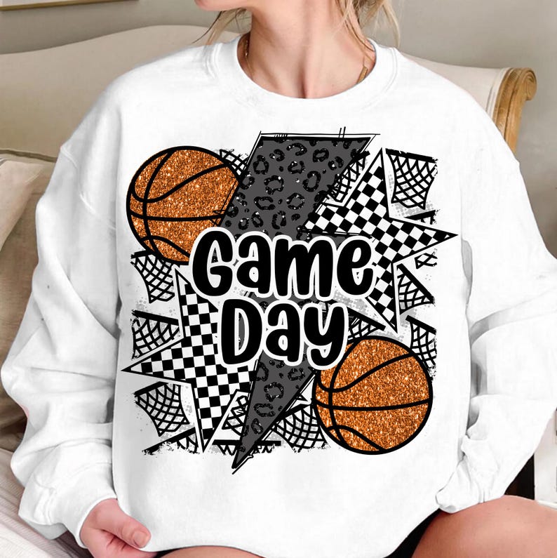 May include: White sweatshirt with a graphic design featuring two basketballs, a chequered star, a leopard print lightning bolt, and the text "Game Day".