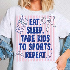 May include: White t-shirt with a pink and white striped background. The shirt features a blue graphic of a drink with ice and a straw, along with the text "EAT. SLEEP. TAKE KIDS TO SPORTS. REPEAT."