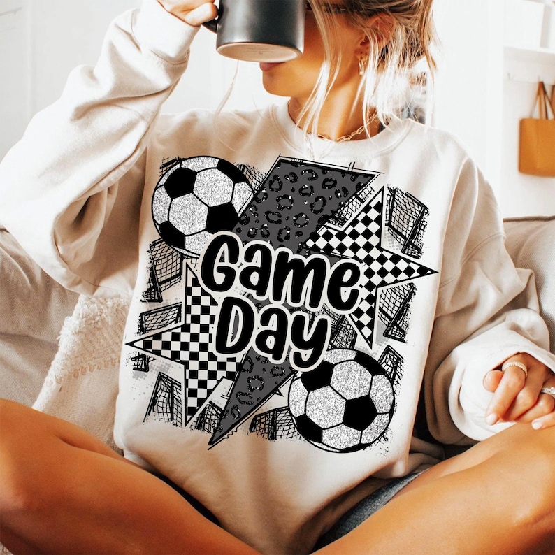 May include: White sweatshirt with a black and white graphic design featuring soccer balls, stars, and the text "Game Day".