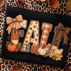 Op de afbeelding: Een zwart sweatshirt met het woord FALL in grote, van stof gemaakte applicatieletters. De letters zijn versierd met diverse herfstpatronen, waaronder ruiten, bladeren en hartjes, geaccentueerd door oranje pompoenen en stoffen strikken.