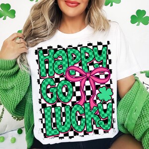May include: White t-shirt with a green and black checkered design. The text "Happy Go Lucky" is written in green letters with a pink bow.