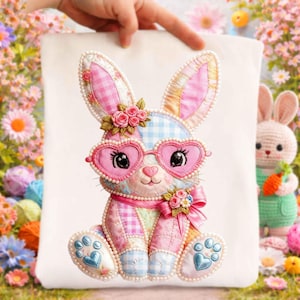 May include: A decorative Easter bunny with heart-shaped glasses, a pink bow, and floral accents. The bunny is made of patchwork fabric in pastel colors, with pearl embellishments. The image is held up by a hand, with a background of flowers and a crocheted bunny.