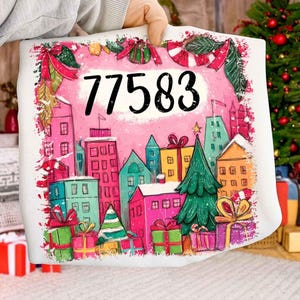May include: A white pillow with a colorful Christmas-themed design. The design features a pink background with the number "77583" in black, surrounded by a cityscape, gifts, and festive decorations. The pillow is held by a person.