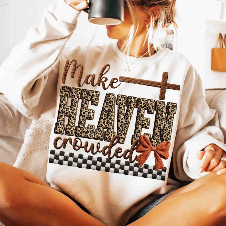 May include: Cream-colored sweatshirt with the phrase "Make Heaven Crowded" in brown and leopard print lettering. A brown cross and bow accent the design. The bottom features a black and white checkered pattern.