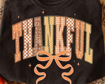 Puede incluir: Sudadera negra de cuello redondo con la palabra "THANKFUL" en letras de patchwork. Las letras presentan varios patrones, incluyendo cuadros, lunares y estrellas. Un lazo naranja está en la parte inferior de la palabra, con pequeños acentos de estrellas.