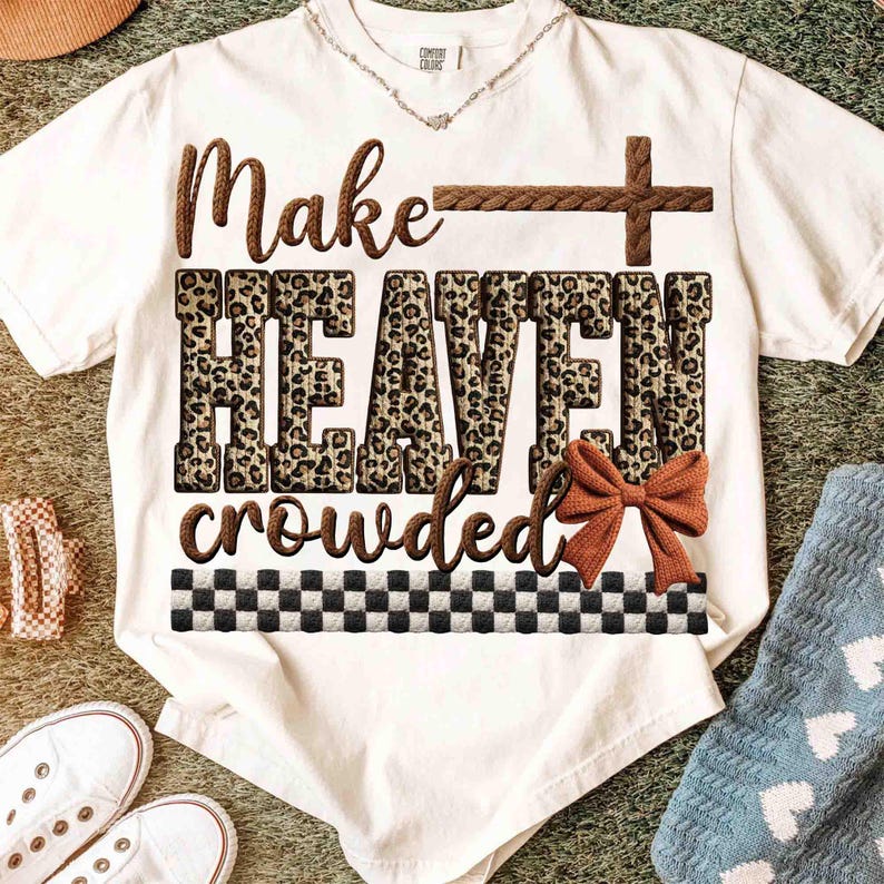 May include: White t-shirt with the text "Make HEAVEN crowded" in brown and leopard print. A brown cross and bow accent the design. The shirt has a black and white checkered pattern at the bottom.