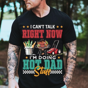 May include: Black t-shirt with the text "I CAN'T TALK RIGHT NOW I'M DOING HOT DAD Stuff". The graphic includes a grill with food, a bucket of beer, and a red lawnmower.