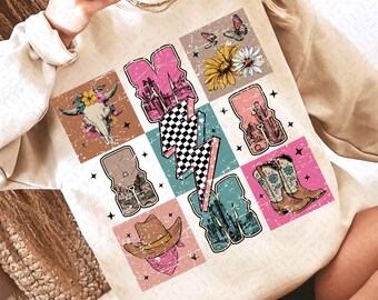 Puede incluir: Una sudadera de color crema con un diseño de inspiración vintage que presenta un rayo a cuadros, botas de vaquero, una calavera con flores y un sombrero de vaquero. Las letras "MAMA" están escritas en bloques de colores.