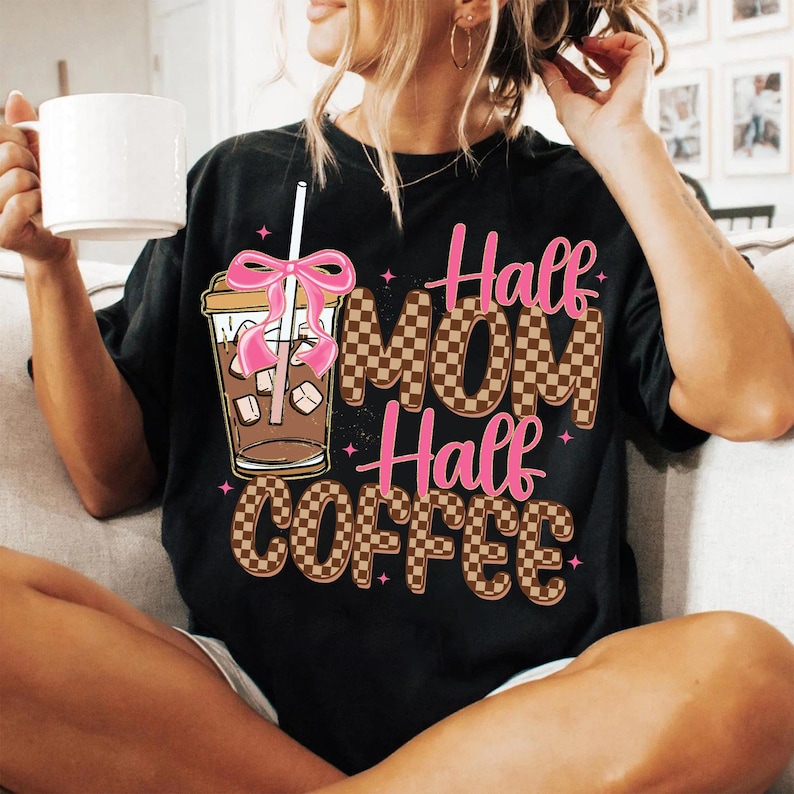 K&ouml;nnte beinhalten: Schwarzes T-Shirt mit braunem und wei&szlig;em Karomuster und dem Text "Half Mom Half Coffee" in Rosa und Braun. Ein rosafarbenes Band befindet sich auf einem Glas mit Eiskaffee und einem Strohhalm.