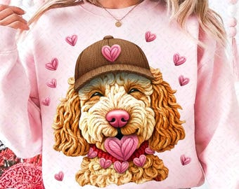 Puede incluir: Sudadera rosa claro con un perro de dibujos animados que lleva una gorra marrón con un corazón rosa. El perro tiene una nariz rosa y una lengua en forma de corazón. Pequeños corazones rosas están esparcidos alrededor del perro.