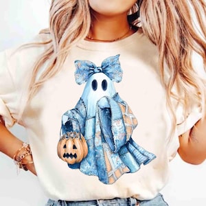 Op de afbeelding: Lichtgekleurd T-shirt met een aquarel illustratie van een spook in een patchwork outfit, met een pompoenemmer. Het spook heeft een blauwe strik en draagt een blauw en oranje patchwork outfit, perfect voor Halloween.