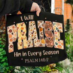 May include: Black t-shirt with the words "I Will PRAISE Him in Every Season" in a fall-themed design. The word "PRAISE" is filled with autumn leaves and pumpkins. The text "PSALM 146:2" is at the bottom.