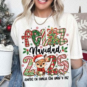 以下が含まれることがあります： クリーム色のTシャツ。クリスマスをテーマにしたデザインで、「Feliz Navidad」の文字が赤と緑のチェック柄で描かれ、クリスマスツリー、サンタ帽をかぶったトナカイ、数字の「225」が描かれています。「Juntos en Familia con Amor y Paz」の文字も含まれています。