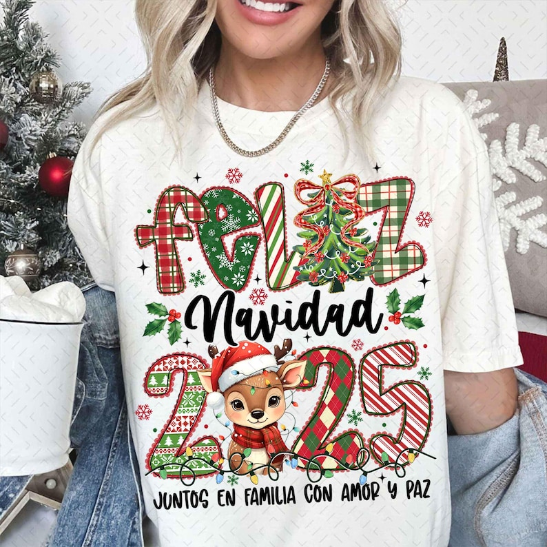 以下が含まれることがあります： クリーム色のTシャツ。クリスマスをテーマにしたデザインで、「Feliz Navidad」の文字が赤と緑のチェック柄で描かれ、クリスマスツリー、サンタ帽をかぶったトナカイ、数字の「225」が描かれています。「Juntos en Familia con Amor y Paz」の文字も含まれています。