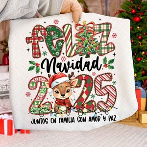 以下が含まれることがあります： 「Feliz Navidad」と「2025」の文字が祝祭的なフォントで描かれた、白いクリスマスをテーマにした枕。サンタ帽をかぶったトナカイ、クリスマスツリー、ストリングライトのデザイン。テキスト「Juntos en familia con amor y paz」も含まれています。