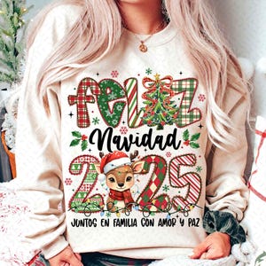 以下が含まれることがあります： クリーム色のスウェットシャツ。お祝いのクリスマスのデザイン。デザインには「Feliz Navidad」と「2025」の文字、サンタ帽をかぶったトナカイ、クリスマスツリー、装飾要素が含まれています。「Juntos en familia con amor y paz」のテキストも含まれています。