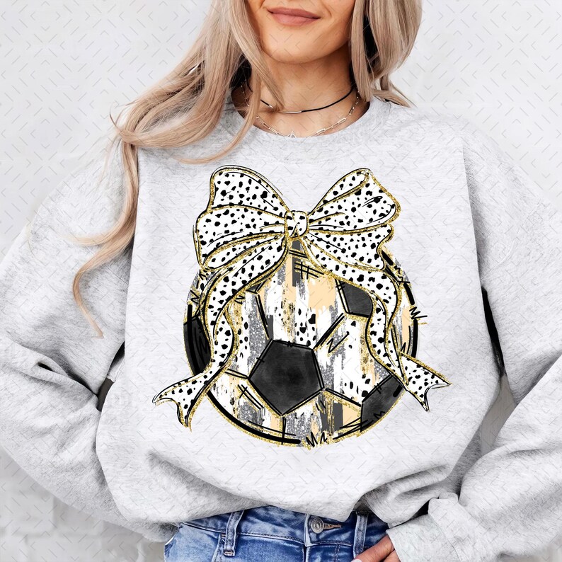 Op de afbeelding: Een grijs sweatshirt met een zwart-witte voetbal met een gouden glitterontwerp en een zwart-witte stippenstrik met gouden glitteraccenten.