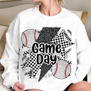 May include: White sweatshirt with a black and white graphic design featuring baseballs, stars, and the text "Game Day".