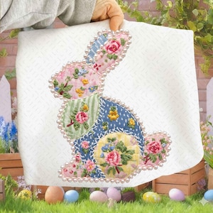 May include: A white fabric square featuring a patchwork bunny design. The bunny is composed of floral patterned fabric pieces in pink, blue, and green, outlined with faux pearls. The design is held by a person.