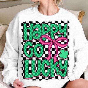 May include: White sweatshirt with a green and black checkered pattern and the text "Happy Go Lucky" in green letters with a pink bow and a green shamrock.