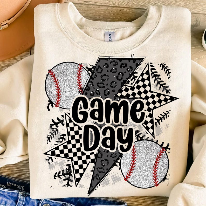 May include: A cream-colored sweatshirt with a graphic design featuring two baseballs, a black and white checkered star, and the text "Game Day".